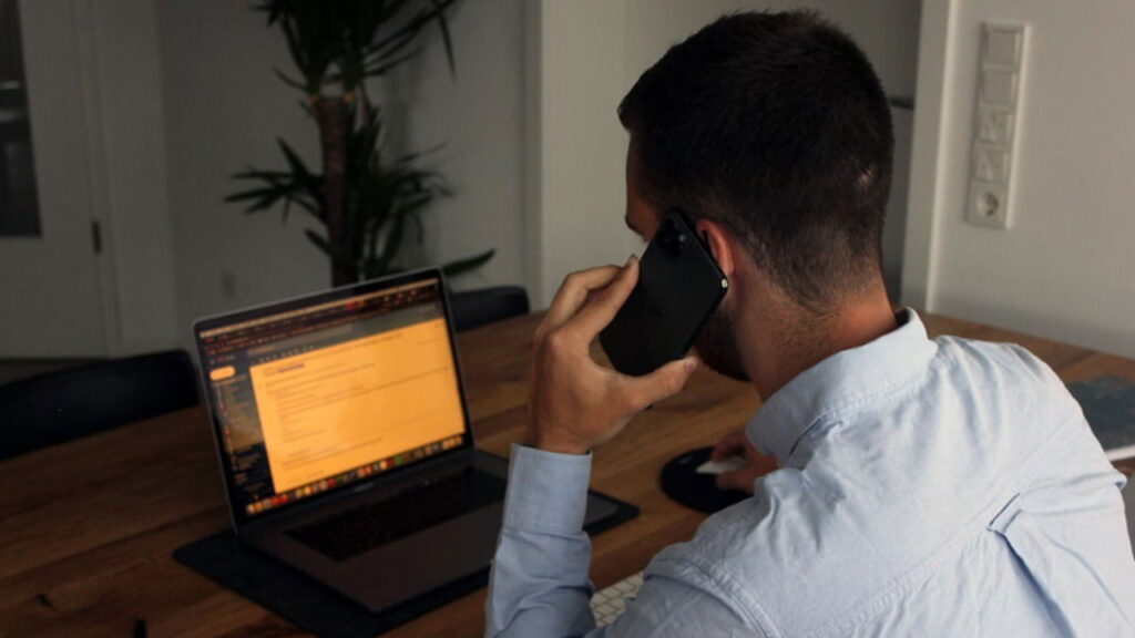 Man calling a number while using a laptop.