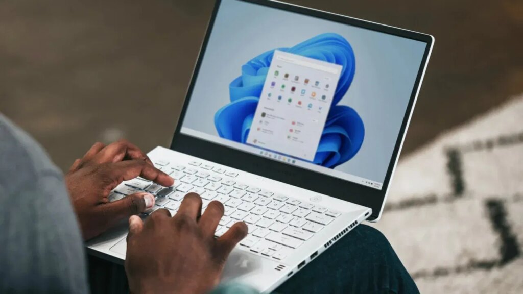 A man using a Windows 11 laptop on his lap with start menu and taskbar showing