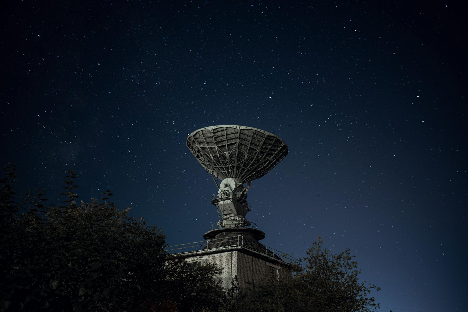 Radiotélescope et arbres verts luxuriants sous un ciel bleu avec des étoiles la nuit