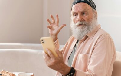 Elderly man with beard and bandana, reacting to smartphone while seated indoors.